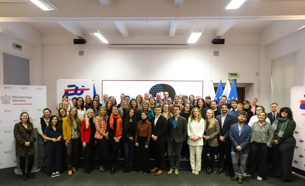 Group photo of TEHDAS2 partners posing in front of a backdrop featuring the Polish Presidency, Ministry of Health, and TEHDAS2 banners, along with EU and Polish flags.